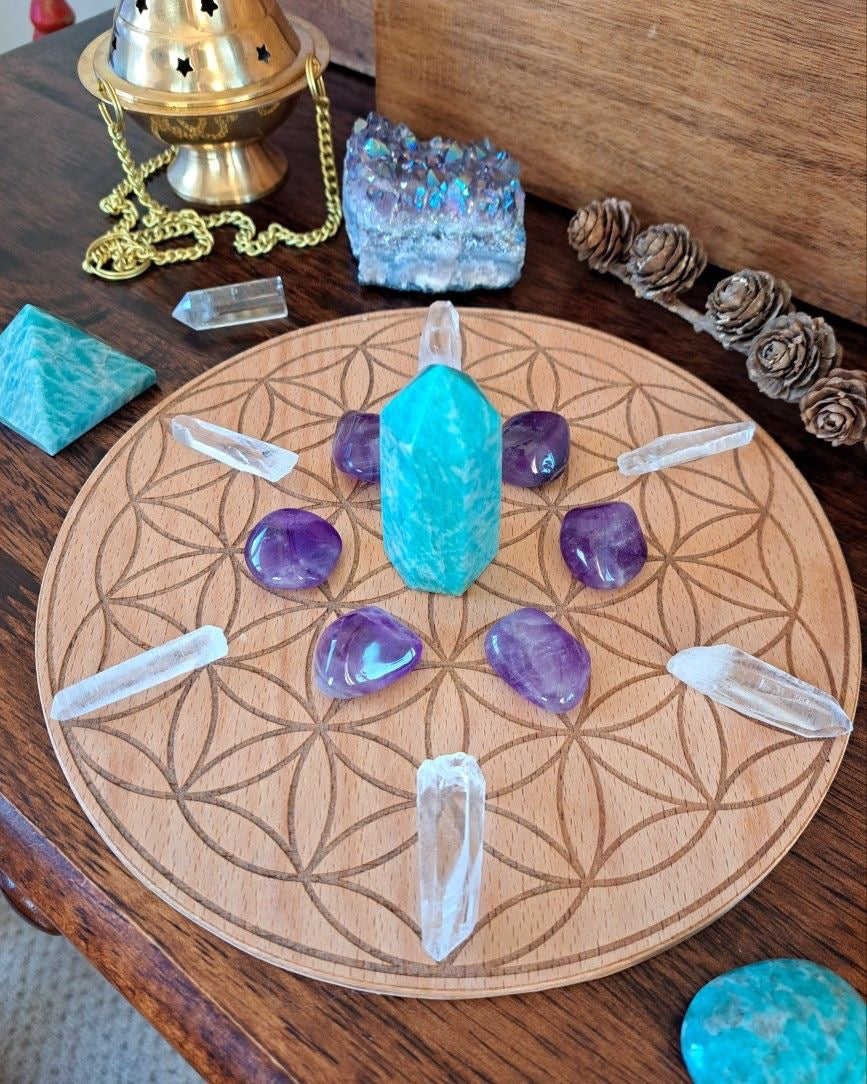 A crystal grid with a bright blue centre stone, purple tumbles and clear quartz points arranged on a patterned wooden board