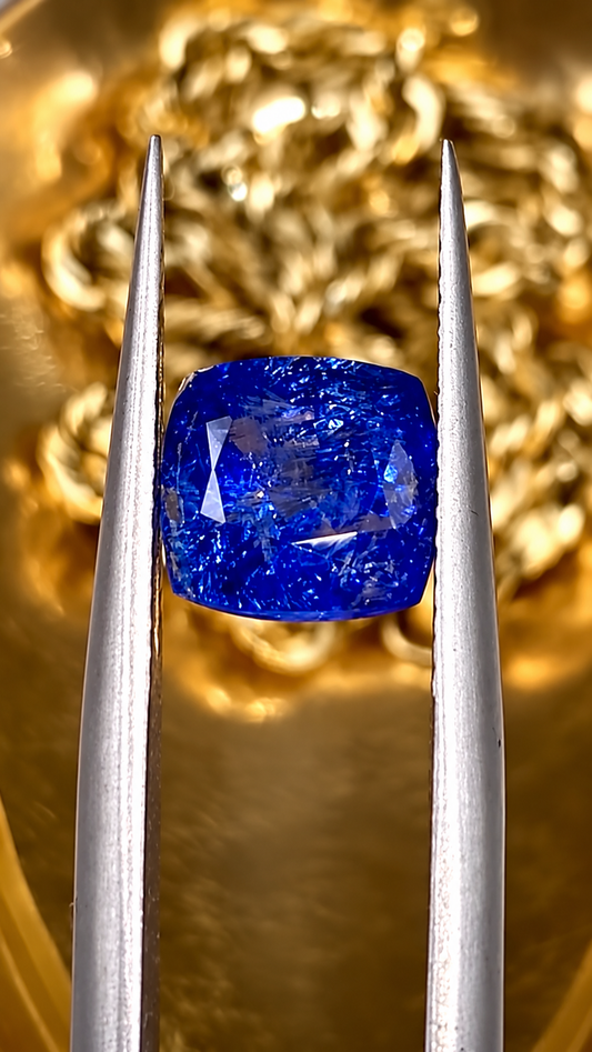 Deep blue sapphire gemstone held in jeweller's tweezers against a warm gold background