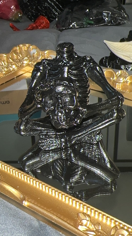 Black 3D printed headless skeleton holding a skull in its arms